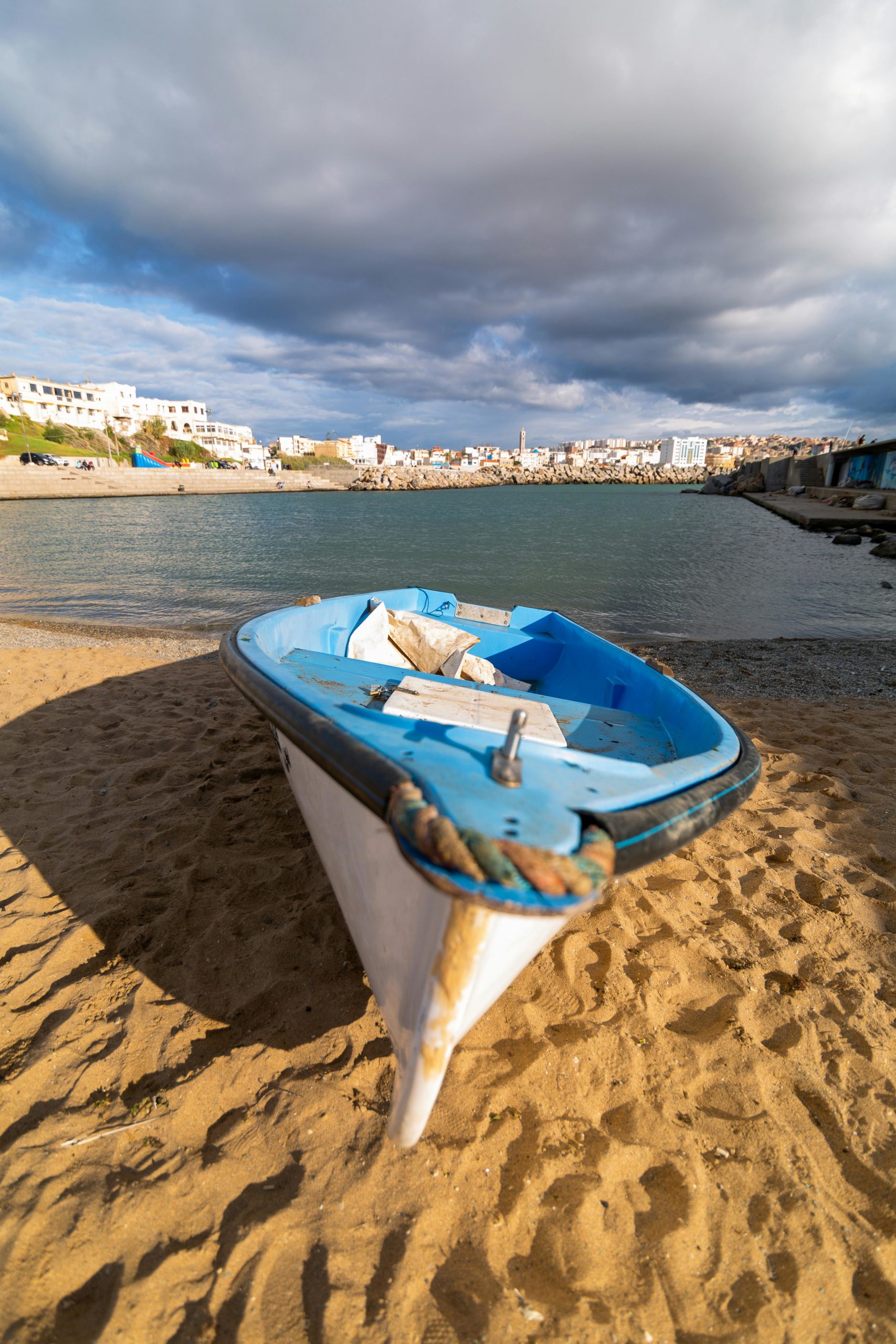 Small boat on sandy beach with cityscape in Algiers, Algeria in the background.