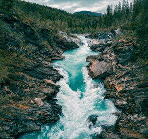 A breathtaking aerial view of a turquoise river rushing through a rocky canyon surrounded by lush forest.